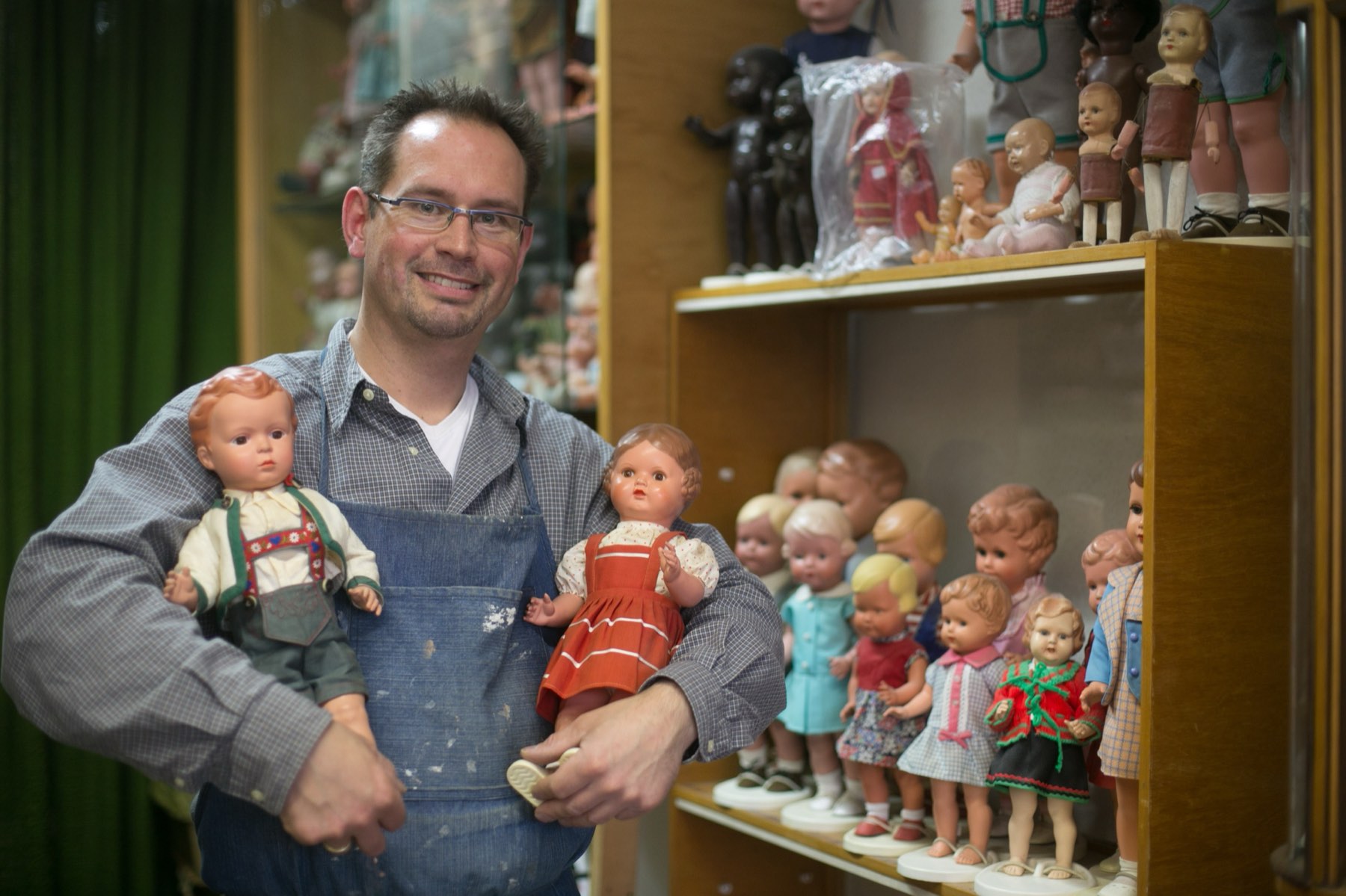 Christian Schneider mit zwei Puppen vor einer Vitrine in der Puppenklinik